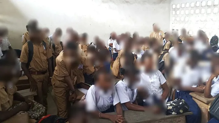 Une classe nombreuse en uniforme écoute la présentation. Visages floutés.